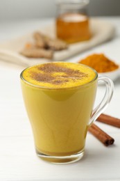 Photo of Tasty turmeric latte in cup and ingredients on white wooden table, closeup