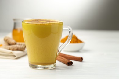 Photo of Tasty turmeric latte in cup and ingredients on white wooden table, closeup. Space for text