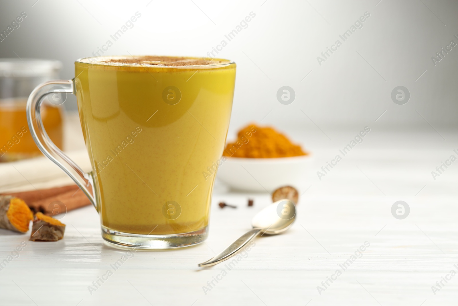 Photo of Tasty turmeric latte in cup and ingredients on white wooden table, closeup. Space for text