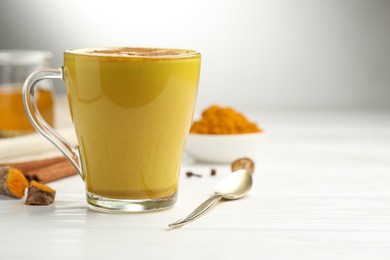 Photo of Tasty turmeric latte in cup and ingredients on white wooden table, closeup. Space for text