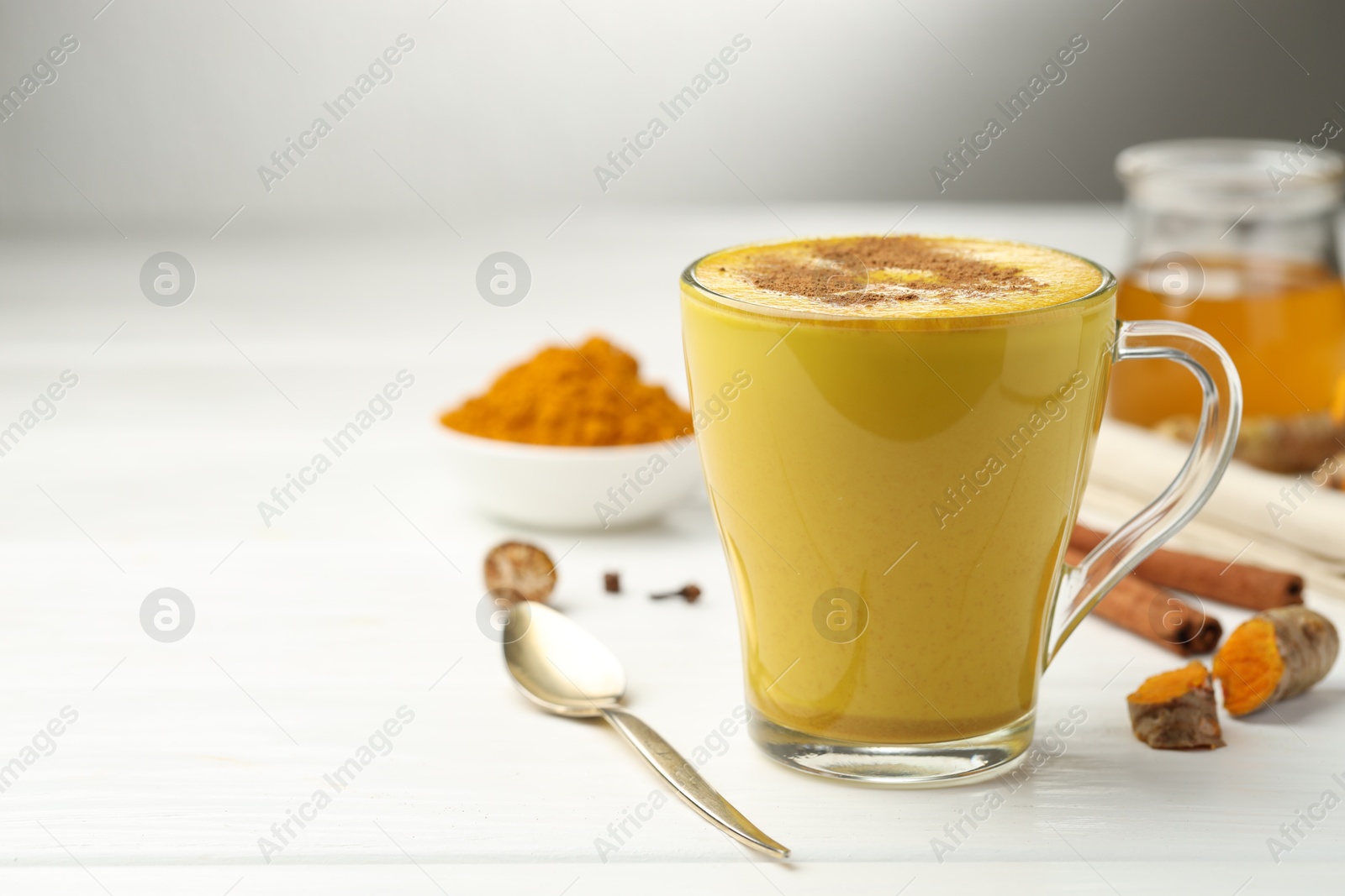 Photo of Tasty turmeric latte in cup and ingredients on white wooden table, closeup. Space for text