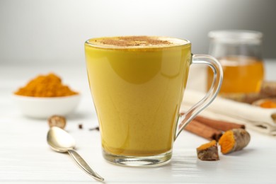 Photo of Tasty turmeric latte in cup and ingredients on white wooden table, closeup