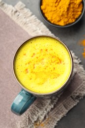 Photo of Tasty turmeric latte in cup and powder on grey table, flat lay