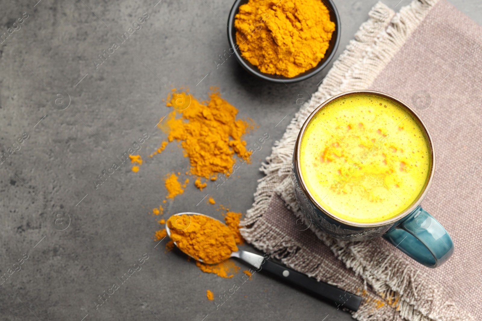 Photo of Tasty turmeric latte in cup and powder on grey table, flat lay. Space for text