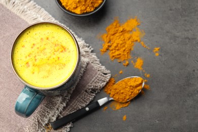 Tasty turmeric latte in cup and powder on grey table, flat lay. Space for text