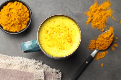 Photo of Tasty turmeric latte in cup and powder on grey table, flat lay