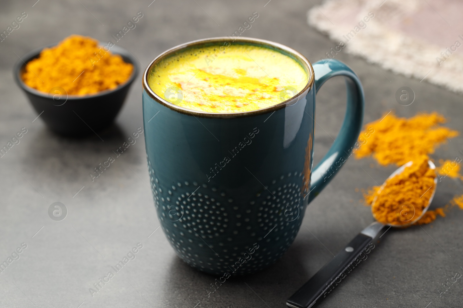 Photo of Tasty turmeric latte in cup and powder on grey table, closeup