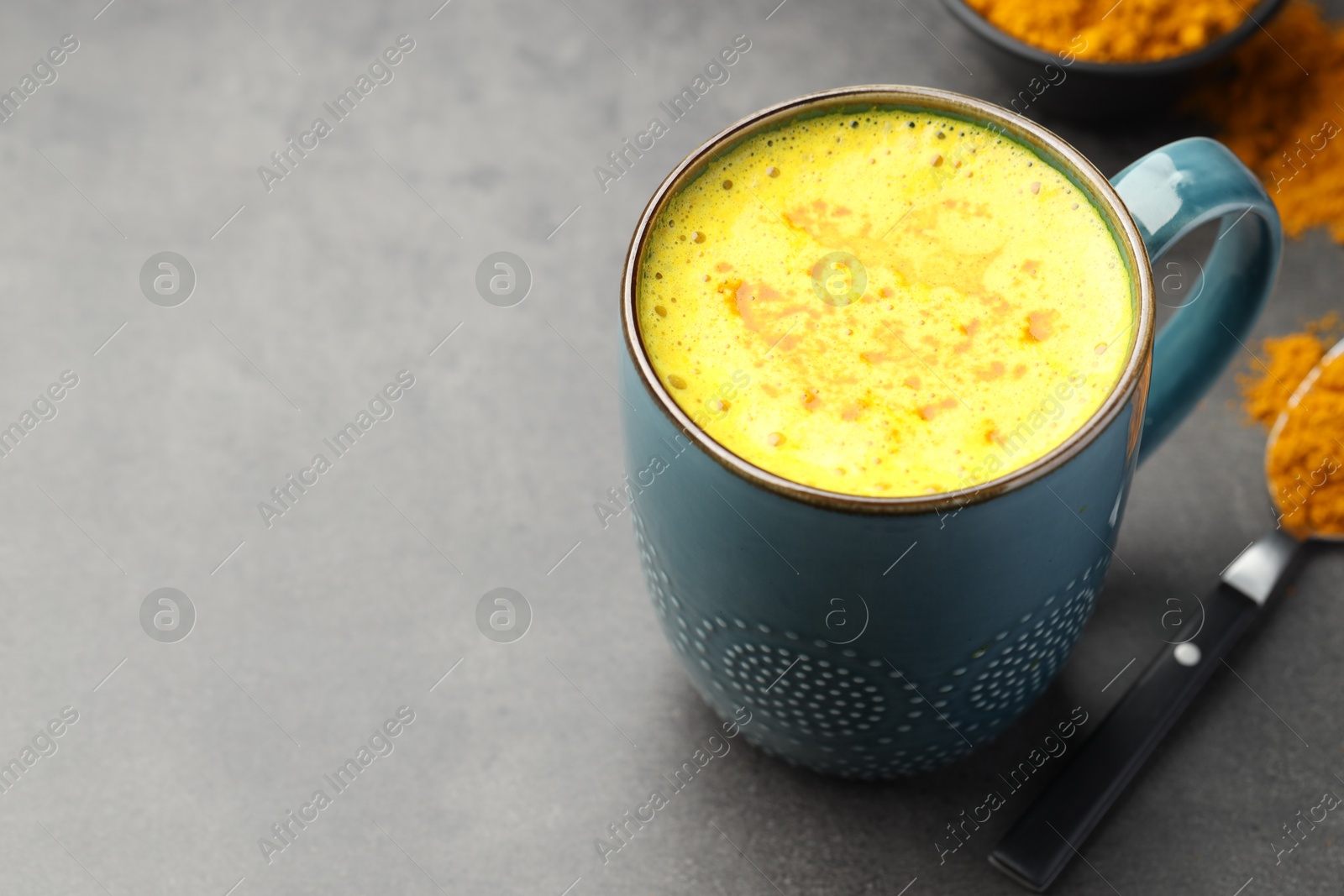 Photo of Tasty turmeric latte in cup and powder on grey table, closeup. Space for text