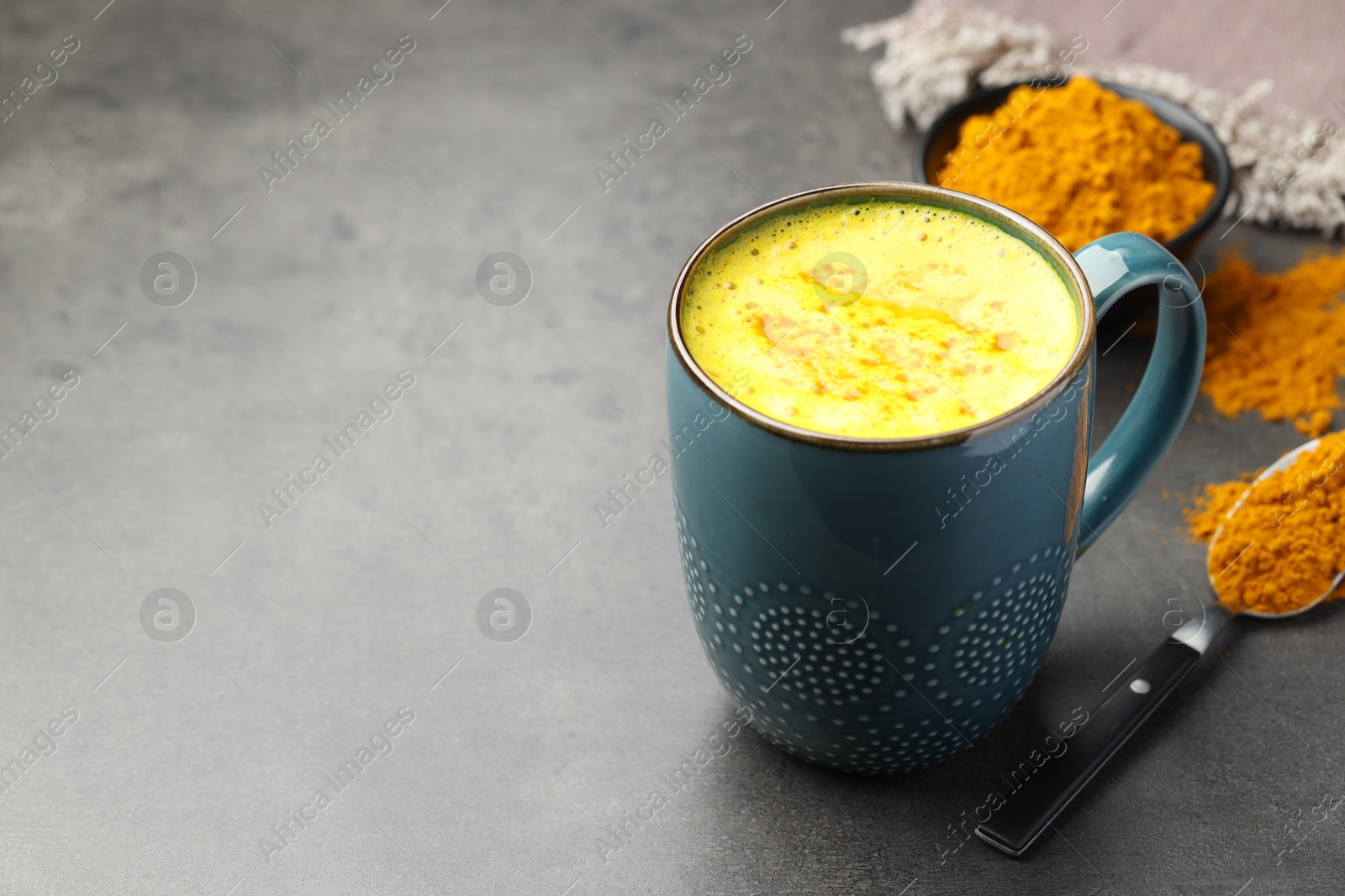 Photo of Tasty turmeric latte in cup and powder on grey table, closeup. Space for text