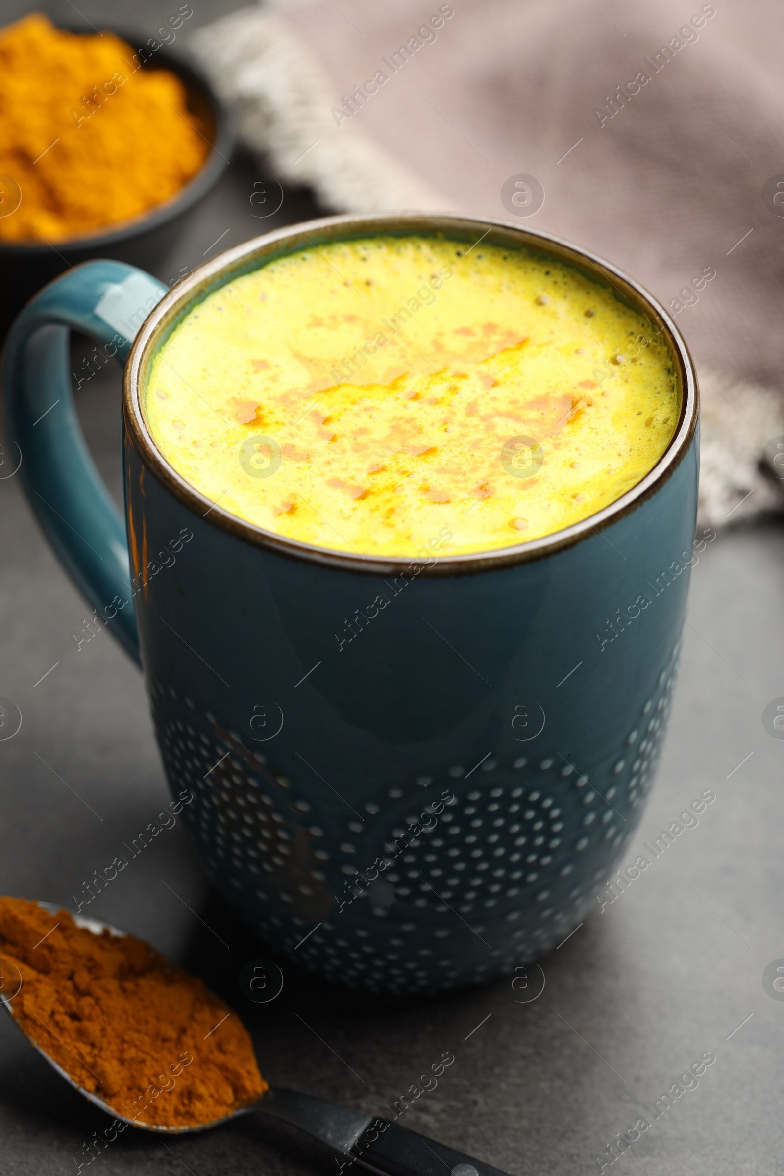 Photo of Tasty turmeric latte in cup and powder on grey table, closeup