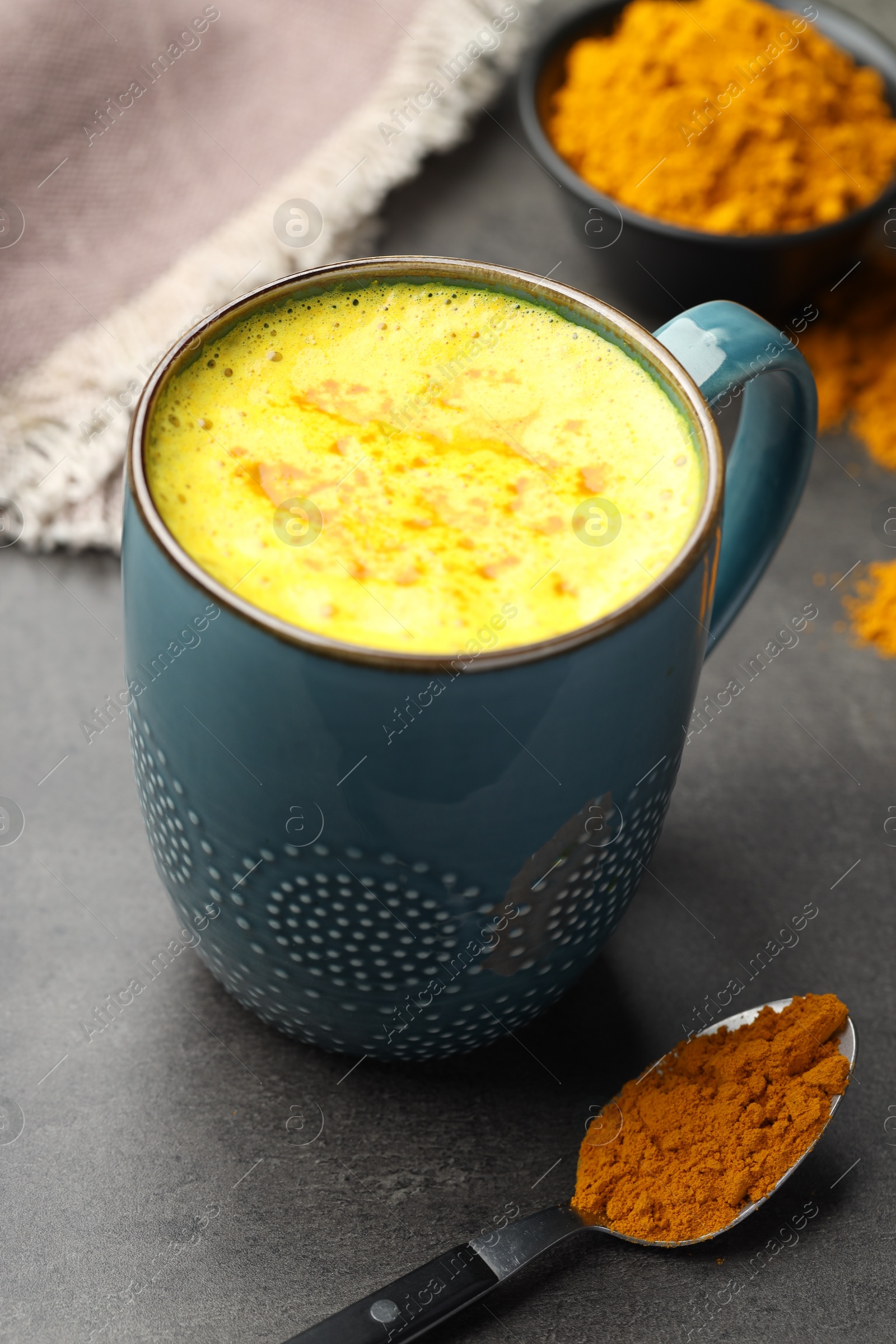 Photo of Tasty turmeric latte in cup and powder on grey table, closeup