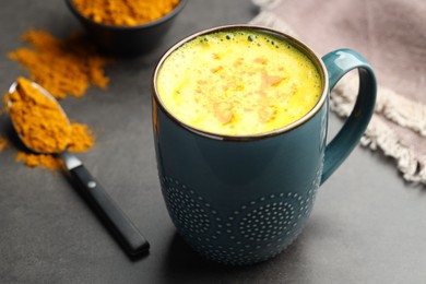 Photo of Tasty turmeric latte in cup and powder on grey table, closeup