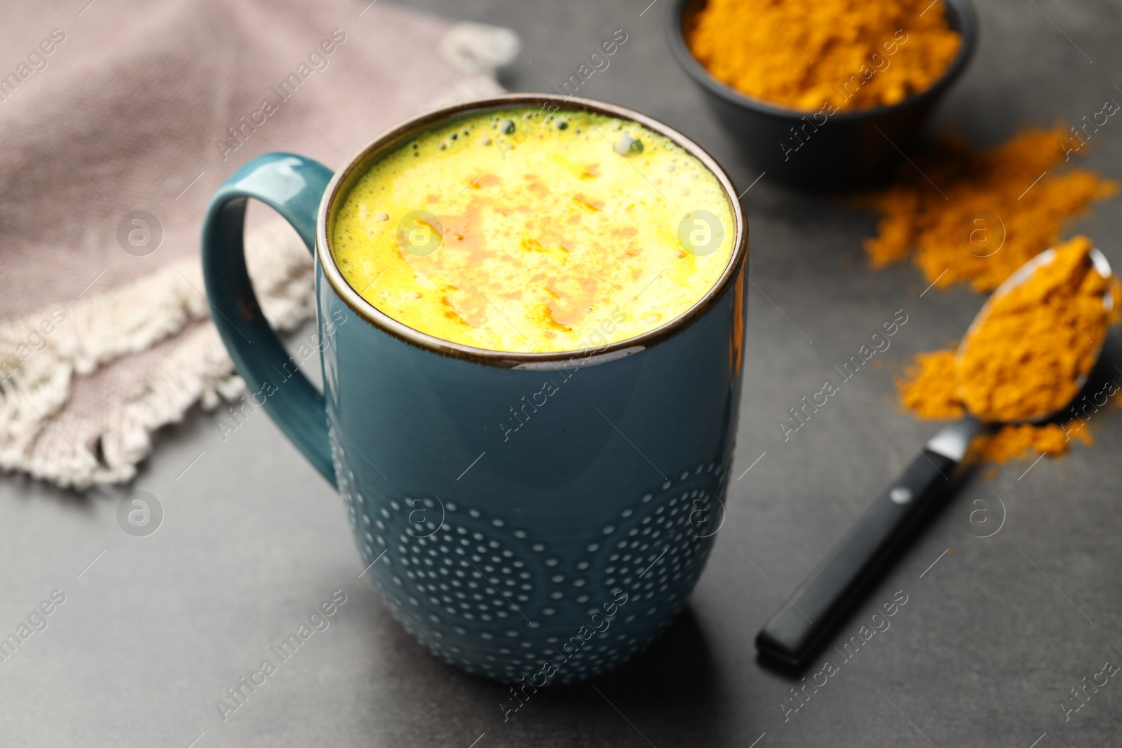 Photo of Tasty turmeric latte in cup and powder on grey table, closeup