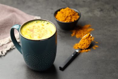 Photo of Tasty turmeric latte in cup and powder on grey table, closeup. Space for text