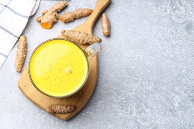 Photo of Tasty turmeric latte in cup and roots on grey table, flat lay. Space for text