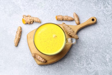 Photo of Tasty turmeric latte in cup and roots on grey table, flat lay