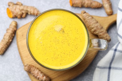 Photo of Tasty turmeric latte in cup and roots on grey table, flat lay