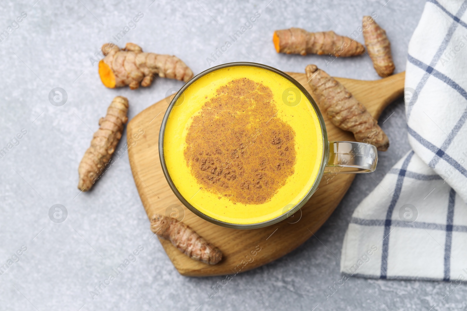 Photo of Tasty turmeric latte in cup and roots on grey table, flat lay