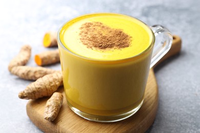 Photo of Tasty turmeric latte in cup and roots on grey table, closeup