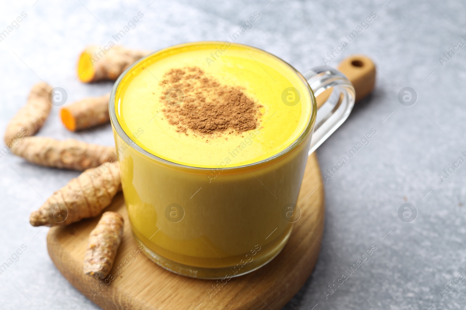 Photo of Tasty turmeric latte in cup and roots on grey table, closeup