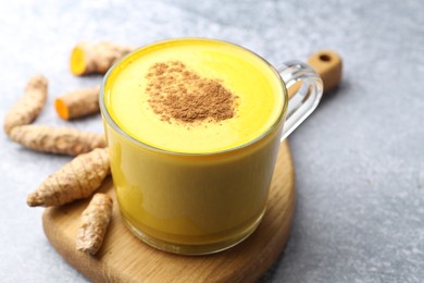 Photo of Tasty turmeric latte in cup and roots on grey table, closeup