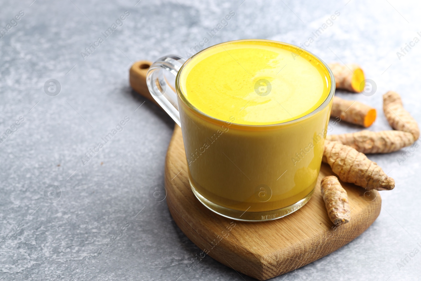 Photo of Tasty turmeric latte in cup and roots on grey table, closeup. Space for text