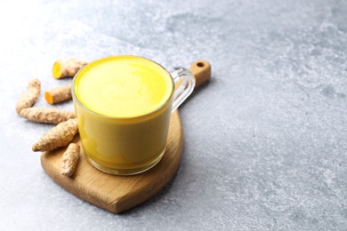 Photo of Tasty turmeric latte in cup and roots on grey table, space for text