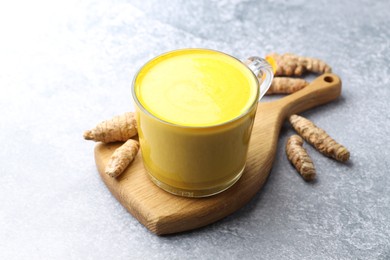 Tasty turmeric latte in cup and roots on grey table