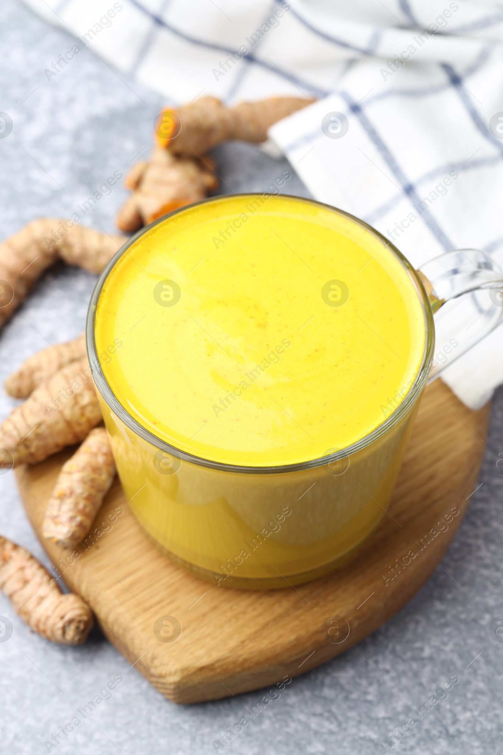 Photo of Tasty turmeric latte in cup and roots on grey table, closeup