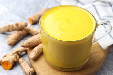 Photo of Tasty turmeric latte in cup and roots on grey table, closeup