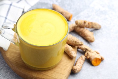 Tasty turmeric latte in cup and roots on grey table, closeup