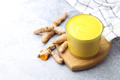 Photo of Tasty turmeric latte in cup and roots on grey table, closeup. Space for text