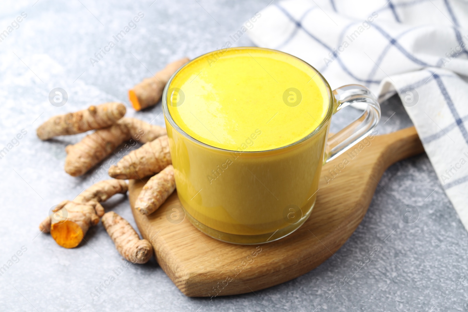 Photo of Tasty turmeric latte in cup and roots on grey table, closeup