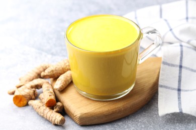 Tasty turmeric latte in cup and roots on grey table, closeup