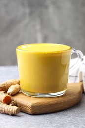 Photo of Tasty turmeric latte in cup and roots on grey table, closeup