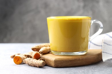 Photo of Tasty turmeric latte in cup and roots on grey table, closeup