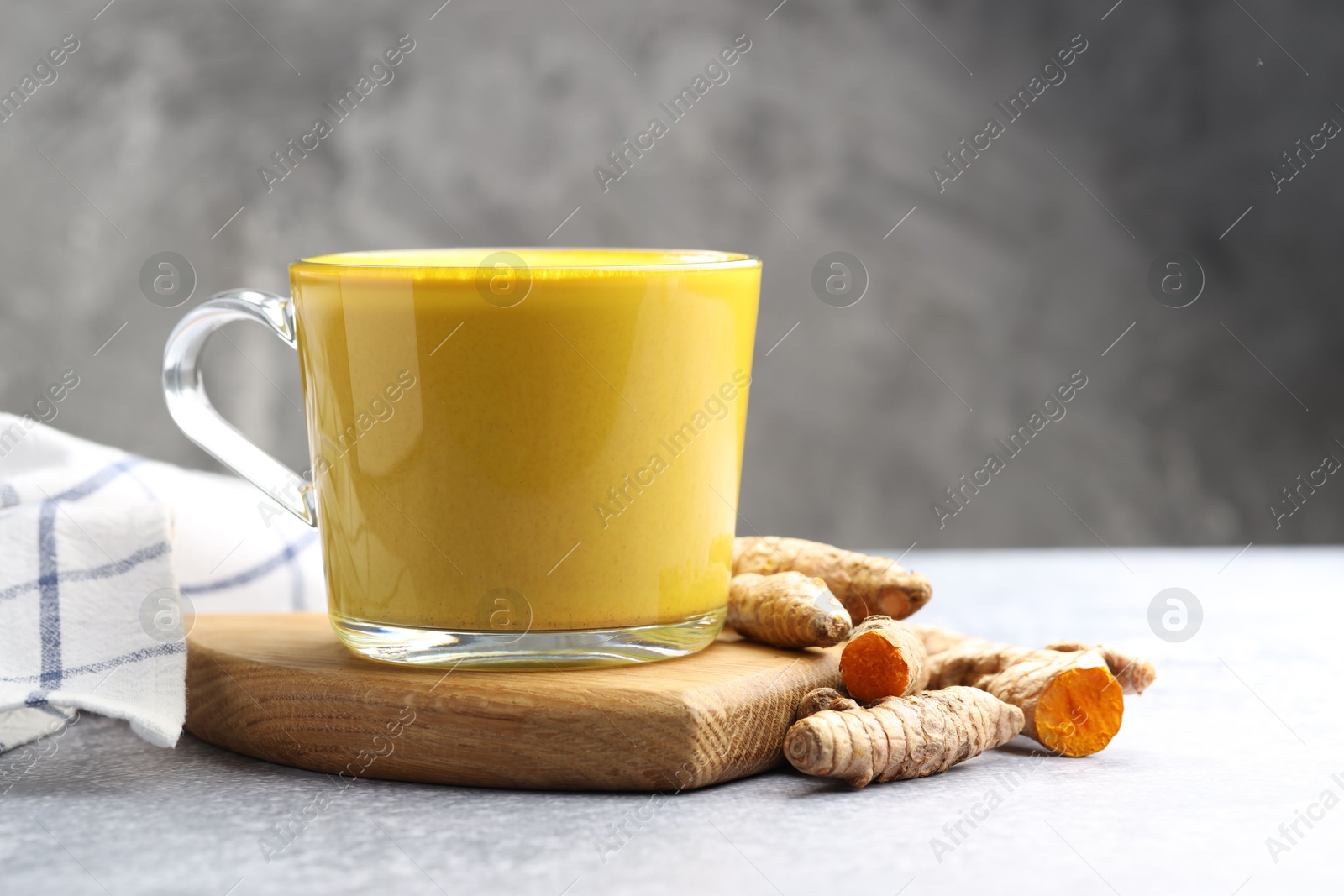 Photo of Tasty turmeric latte in cup and roots on grey table, closeup. Space for text