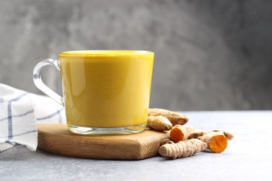 Photo of Tasty turmeric latte in cup and roots on grey table, closeup. Space for text