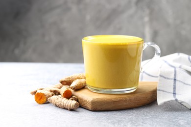 Photo of Tasty turmeric latte in cup and roots on grey table, closeup