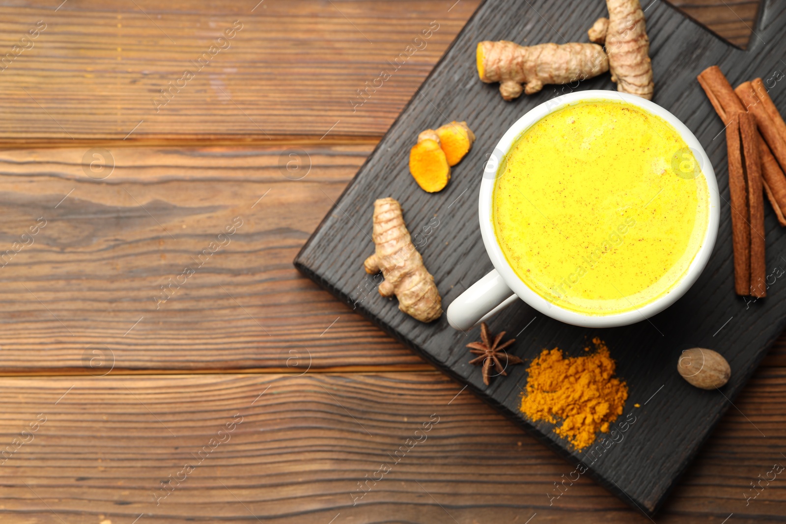 Photo of Tasty turmeric latte in cup and spices on wooden table, flat lay. Space for text