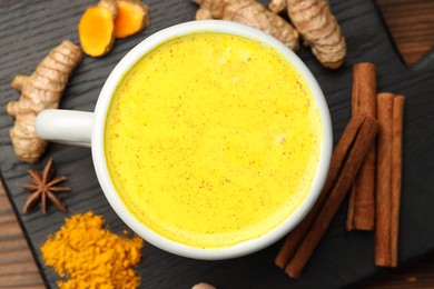 Photo of Tasty turmeric latte in cup and spices on wooden table, flat lay