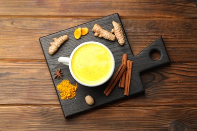 Photo of Tasty turmeric latte in cup and spices on wooden table, flat lay