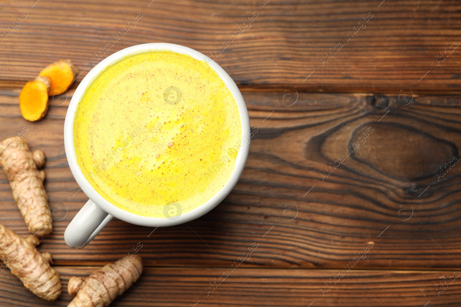 Photo of Tasty turmeric latte in cup and roots on wooden table, flat lay. Space for text