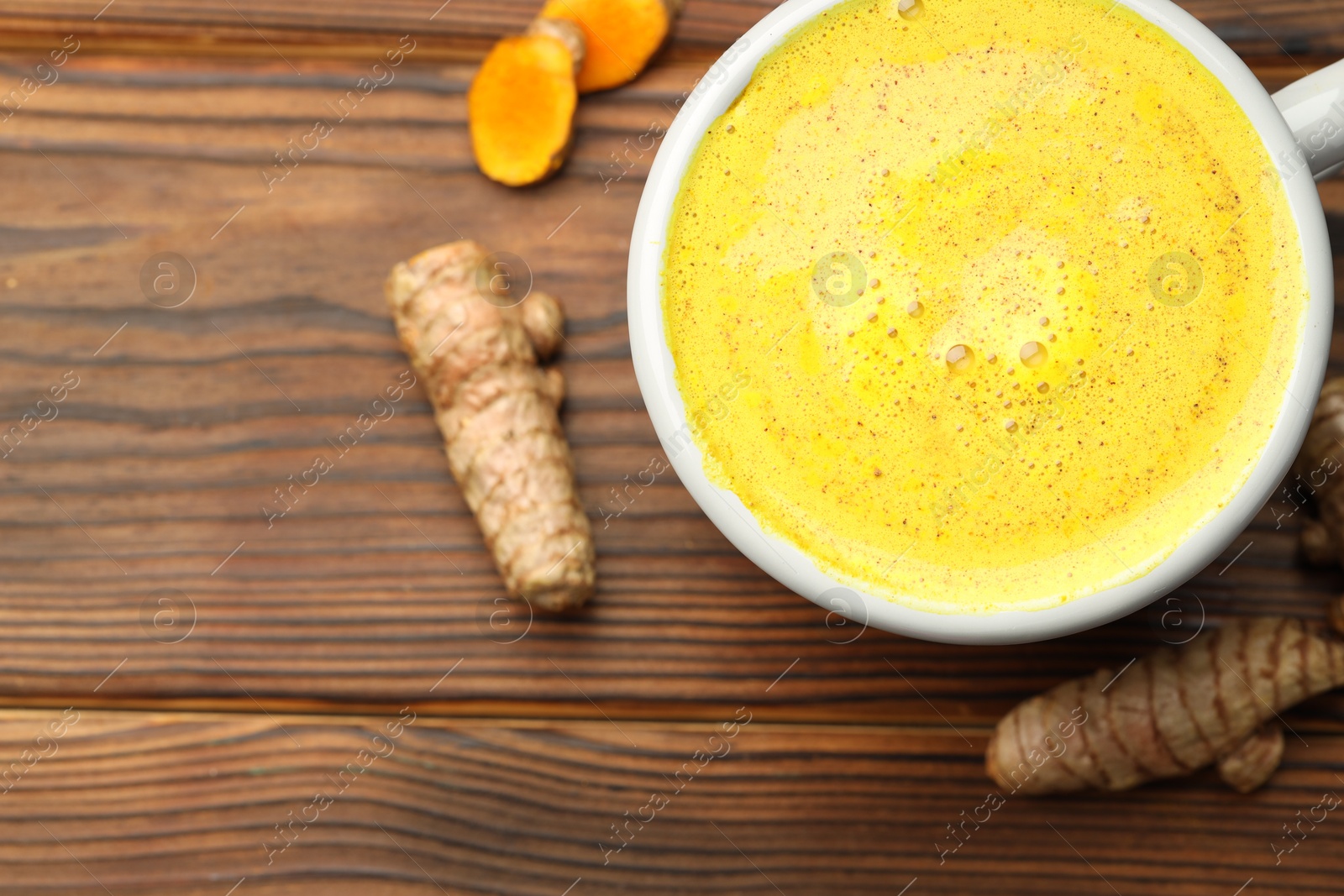 Photo of Tasty turmeric latte in cup and roots on wooden table, flat lay. Space for text