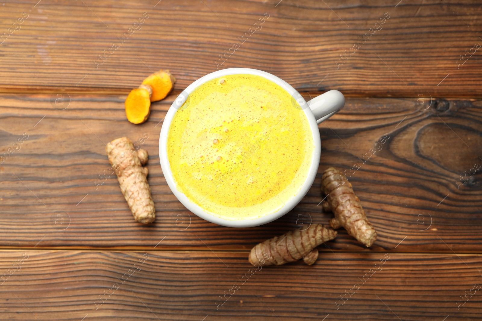 Photo of Tasty turmeric latte in cup and roots on wooden table, flat lay