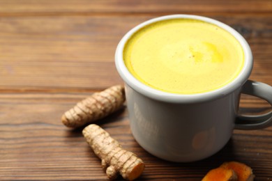 Tasty turmeric latte in cup and roots on wooden table, closeup. Space for text