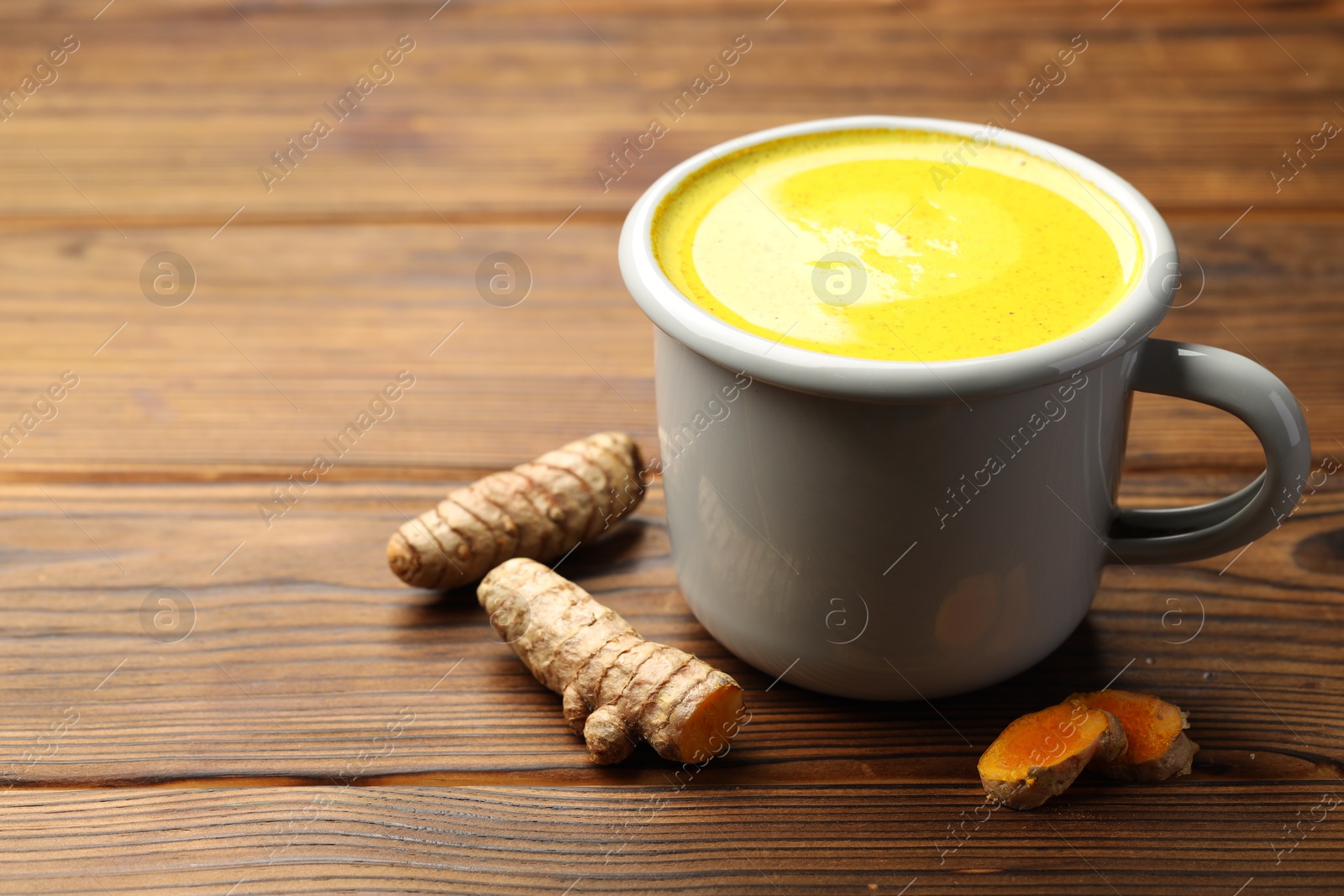 Photo of Tasty turmeric latte in cup and roots on wooden table, closeup. Space for text