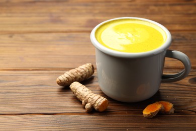 Photo of Tasty turmeric latte in cup and roots on wooden table, closeup. Space for text