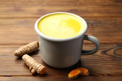 Photo of Tasty turmeric latte in cup and roots on wooden table, closeup