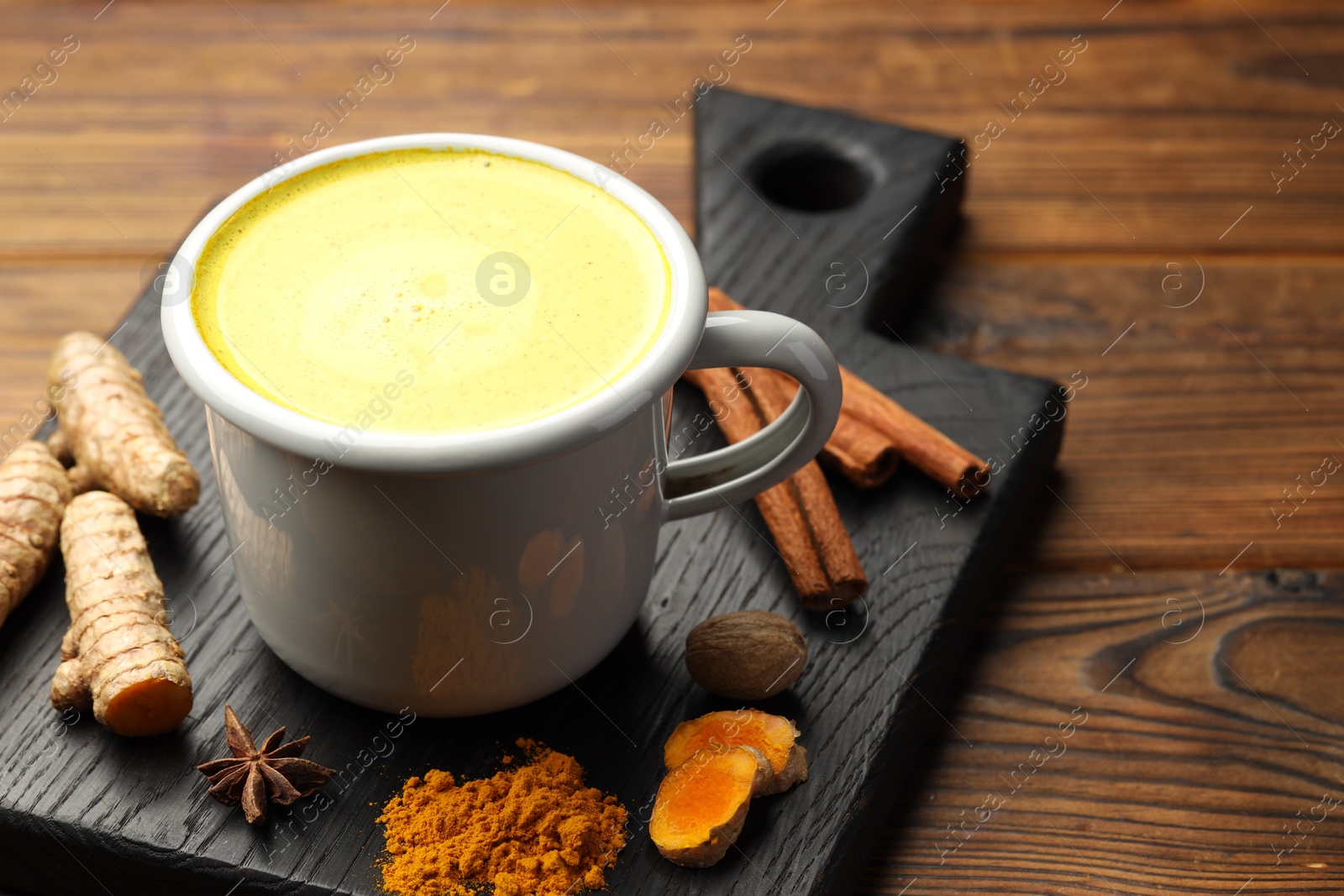 Photo of Tasty turmeric latte in cup and spices on wooden table, closeup